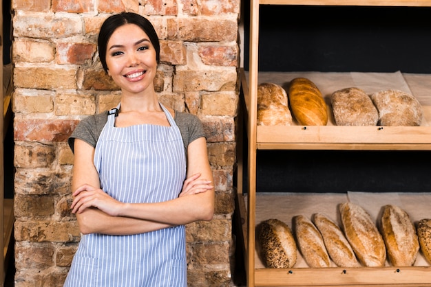 Panadero de sexo femenino confiado que se coloca cerca del estante de madera con panes cocidos