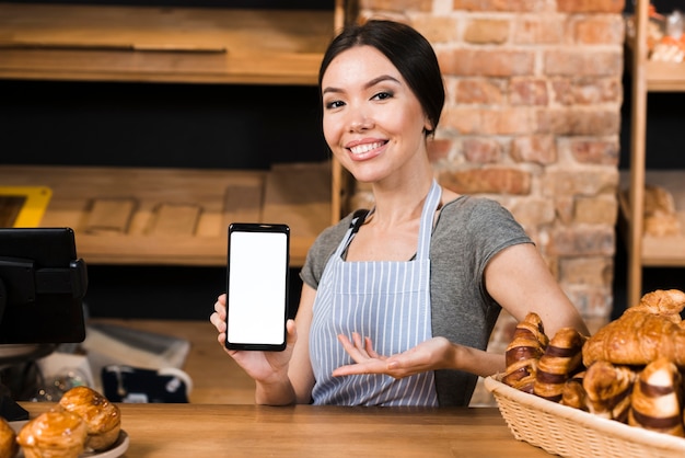 Panadero de sexo femenino confiado sonriente en el contador de la panadería que muestra la exhibición del teléfono móvil
