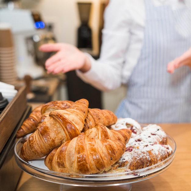 Panadero de sexo femenino que presenta los croissants cocidos en el soporte de la torta.