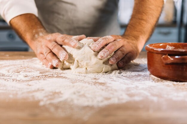 Panadero de sexo masculino amasando la harina de la masa en la mesa de madera