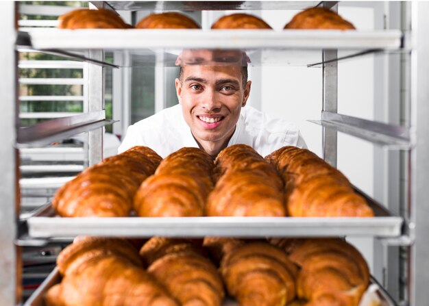 Panadero de sexo masculino de pie detrás de los estantes llenos de croissant recién horneado