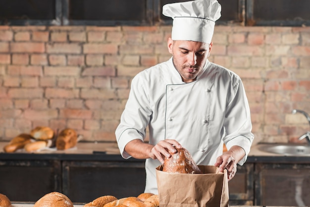 Panadero de sexo masculino que mira panes en bolsa de papel