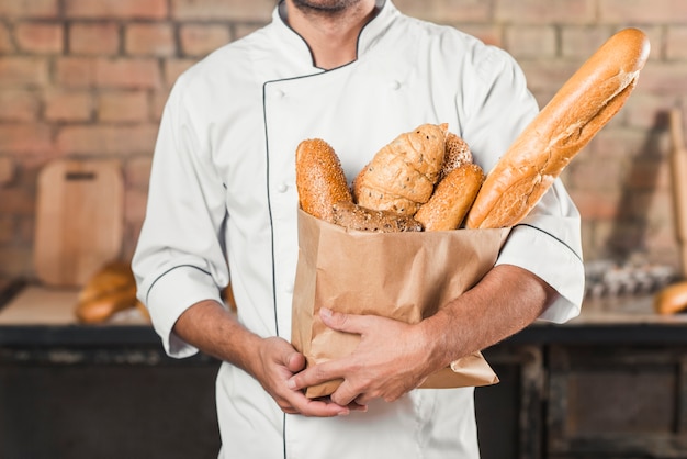 Panadero de sexo masculino que sostiene la bolsa de papel con diversa barra de pan