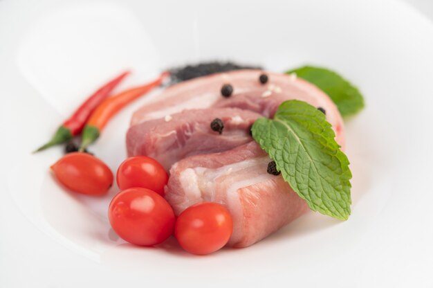 Foto gratuita panceta de cerdo en un plato blanco con semillas de pimiento tomates y especias.