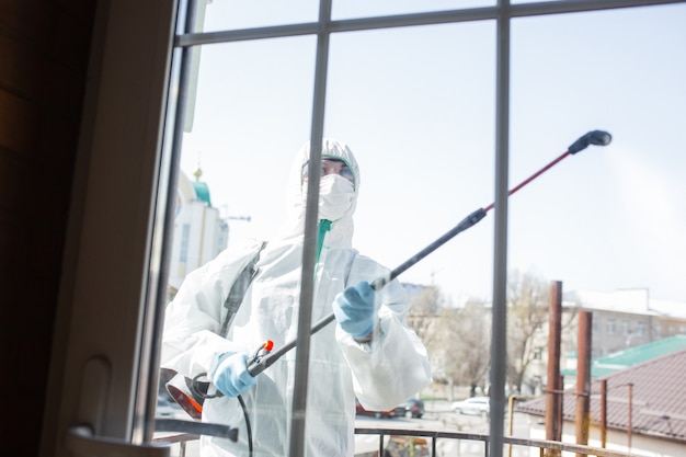 Pandemia de coronavirus. Un desinfectante con un traje protector y una máscara rocía desinfectantes en la habitación.