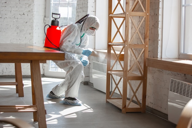 Foto gratuita pandemia de coronavirus. un desinfectante con traje protector y mascarilla rocía desinfectantes en casa u oficina.