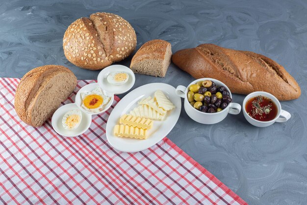 Panes de pan integral y en rodajas alrededor de una configuración de desayuno sobre un mantel sobre una mesa de mármol.