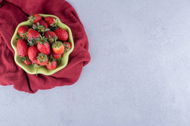 Paño rojo debajo de un cuenco de fresas sobre fondo de mármol. Foto de alta calidad