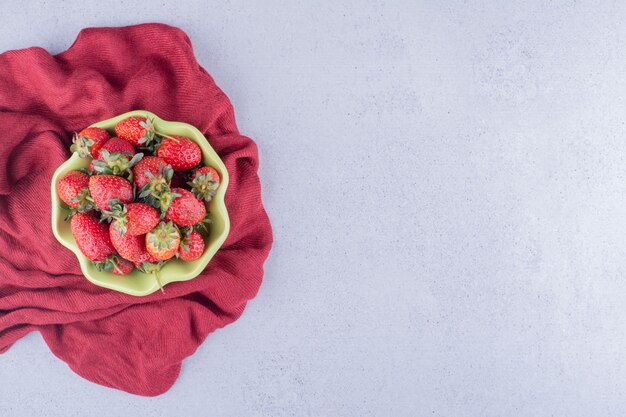 Paño rojo debajo de un cuenco de fresas sobre fondo de mármol. Foto de alta calidad