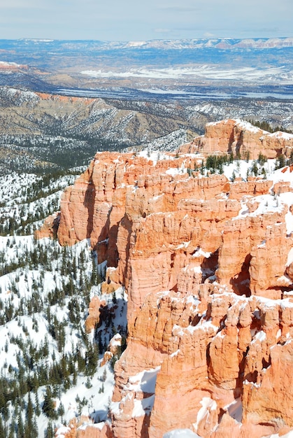 Panorama del cañón Bryce con nieve en invierno con rocas rojas y cielo azul.