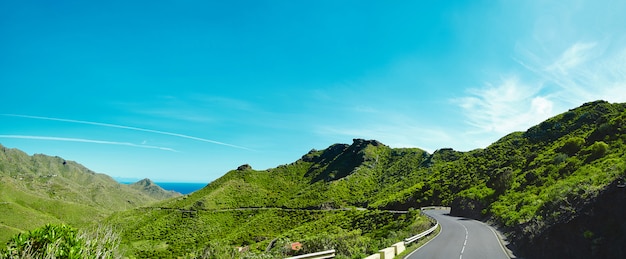 El panorama y la hermosa vista de montañas y el cielo azul con la carretera de asfalto serpentean entre el fiordo azul y las montañas de musgo.