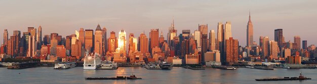 Panorama del horizonte de Manhattan de Nueva York al atardecer con Empire State Building y rascacielos con reflejo sobre el río Hudson.