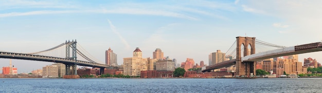 Panorama del Puente de Manhattan y el Puente de Brooklyn sobre el East River visto desde el paseo marítimo del Bajo Manhattan de la ciudad de Nueva York al atardecer.