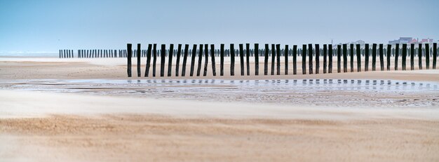 Panorama de tablones de madera verticales en la arena de un muelle de madera sin terminar en la playa en Francia