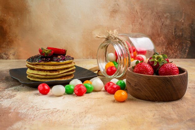 Panqueques dulces de vista frontal con caramelos de colores en la mesa de luz