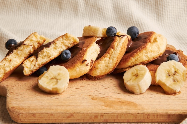 Foto gratuita panqueques con salsa de chocolate, bayas y plátano en una placa de madera