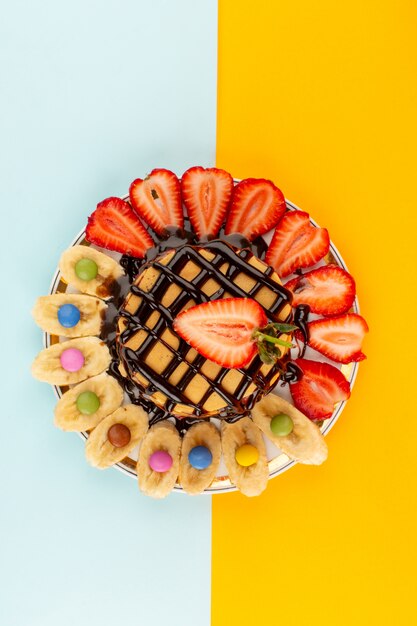 Panqueques de la vista superior junto con fresas rojas en rodajas y plátanos diseñados dentro de un plato blanco