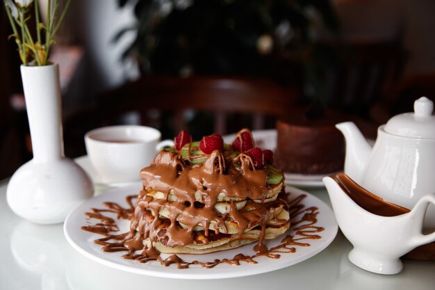 Panqueques de waffle de vista frontal con plátanos, kiwi y fresas con chocolate vertido encima en un plato
