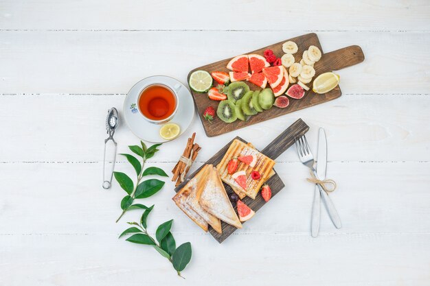 Panqueques y waffles sobre tabla de madera con té y frutas