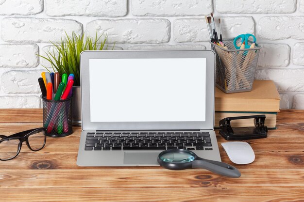 Pantalla en blanco del ordenador portátil del espacio de trabajo en la mesa de madera