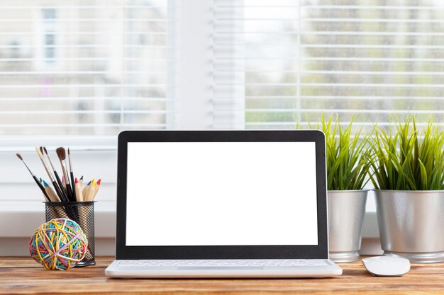 Pantalla en blanco del ordenador portátil del espacio de trabajo en la mesa de madera