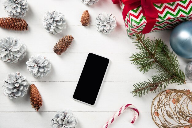 Pantalla vacía en blanco del teléfono inteligente en la pared de madera blanca con decoración y regalos coloridos de vacaciones.