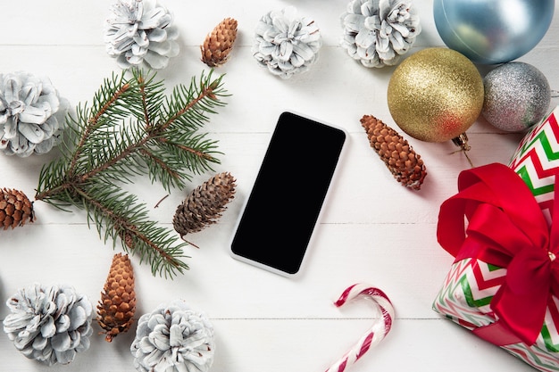 Pantalla vacía en blanco del teléfono inteligente en la pared de madera blanca con decoración y regalos coloridos de vacaciones.