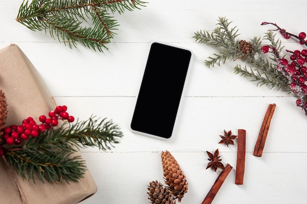 Pantalla vacía en blanco del teléfono inteligente en la pared de madera blanca con decoración y regalos coloridos de vacaciones.