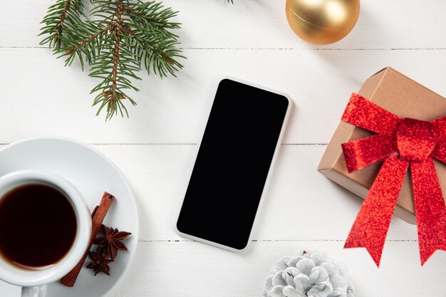 Pantalla vacía en blanco del teléfono inteligente en la pared de madera blanca con decoración y regalos coloridos de vacaciones.