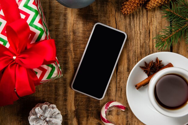 Pantalla vacía en blanco del teléfono inteligente en la pared de madera con decoración colorida, té y regalos.