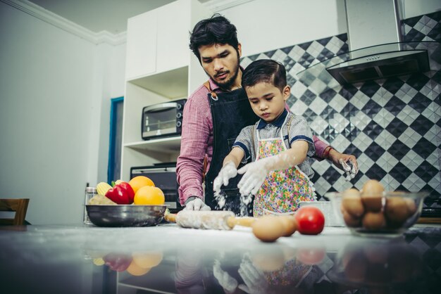 Papá enseña a su hijo a cocinar en la cocina en casa. Concepto de familia