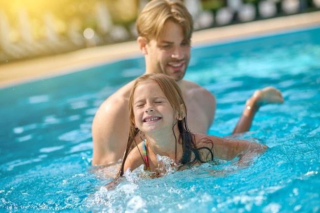 Papá enseñando a su hija a nadar en una piscina