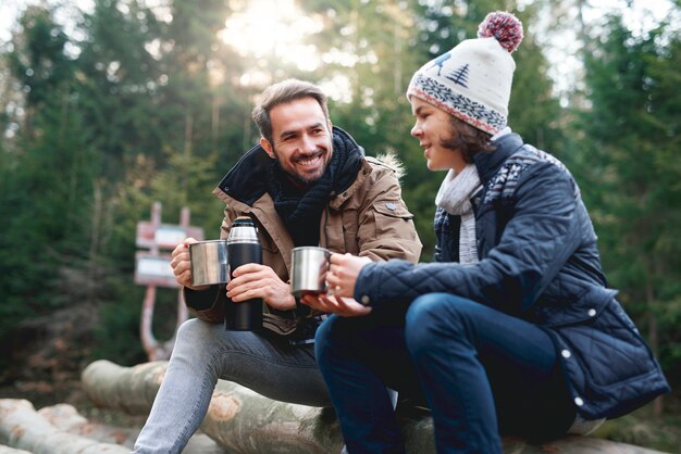 Papá feliz y su hijo bebiendo té en el bosque de otoño