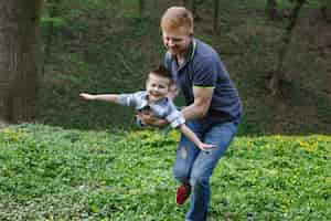 Foto gratuita papá gira a su hijo como un avión jugando en el parque verde