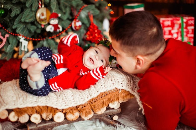 Foto gratuita papá se inclina hacia su pequeña hija mientras ella yace ante un árbol de navidad