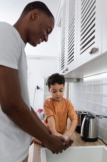 Papá joven lavando platos con su hijo