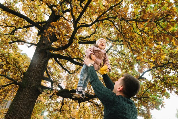 Papá levantando a su hija sonriente en el bosque de otoño