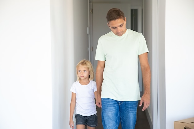 Papá llevando a su hija bonita a su nuevo apartamento, tomados de la mano, caminando en el pasillo
