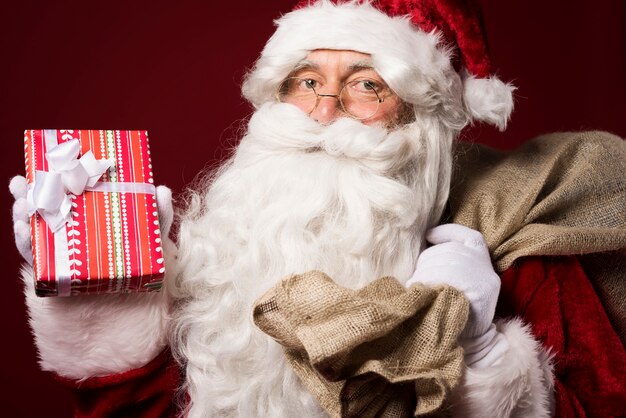 Papá Noel con una caja de regalo sobre fondo rojo.