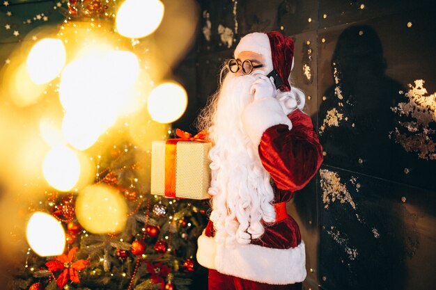 Papá Noel hablando por teléfono y sosteniendo un regalo.