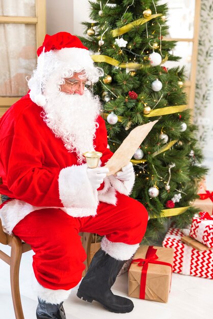 Papá Noel leyendo papel cerca de árbol de navidad