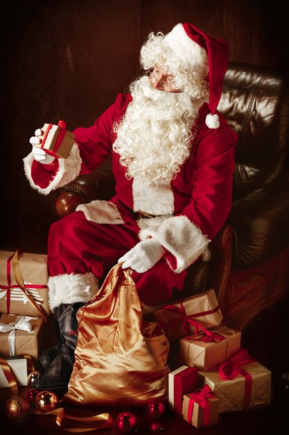 Papá Noel con una lujosa barba blanca, sombrero de Papá Noel y un traje rojo sentado con regalos