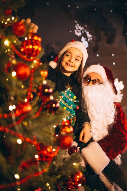 Papá Noel con la niña que adorna el árbol de navidad junto