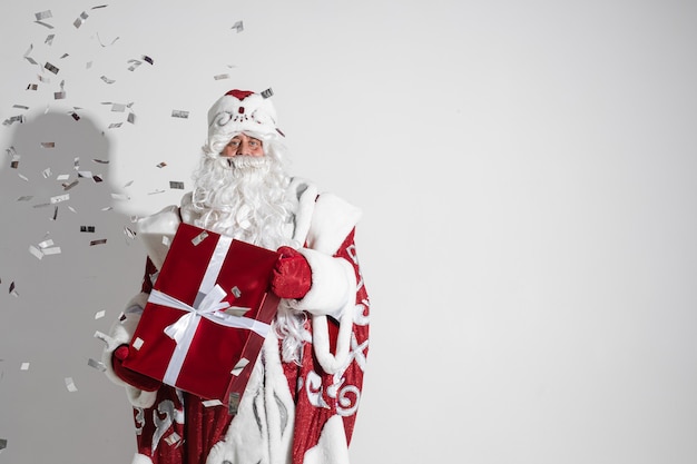 Papá Noel sosteniendo un regalo de Navidad envuelto bajo una lluvia de confeti plateado.