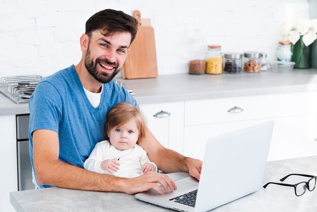 Papá sonriendo mientras trabajaba en la computadora portátil con bebé