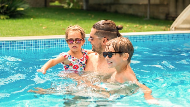 Papá sosteniendo a su feliz hija e hijo en sus manos en la piscina