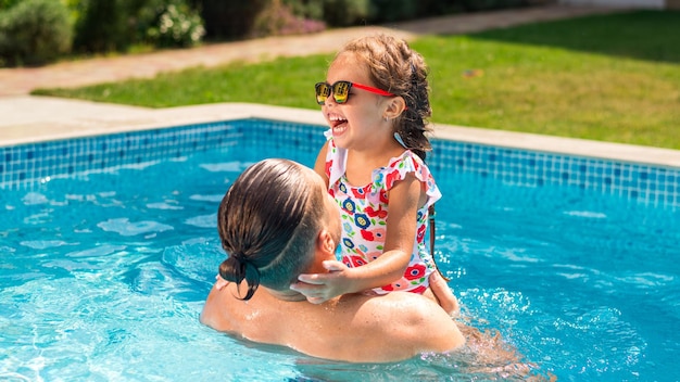 Papá sosteniendo a su hija feliz en sus manos en la piscina