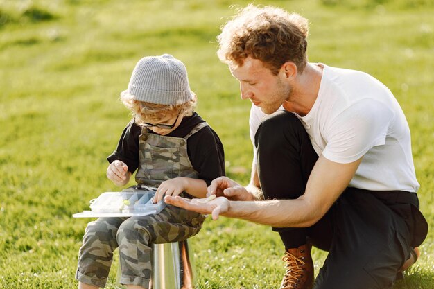 Papá y su hijo pasan tiempo juntos al aire libre. Niño rizado vistiendo un mono de color caqui. Niño sentado en un balde y escuchando a su padre