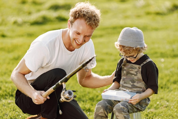 Papá y su hijo pasan tiempo juntos al aire libre. Niño rizado vistiendo un mono de color caqui. Niño sentado en un balde y escuchando a su padre