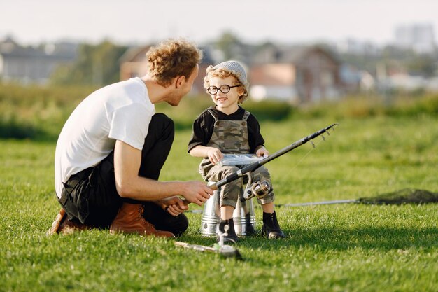 Papá y su hijo pasan tiempo juntos al aire libre. Niño rizado vistiendo un mono de color caqui. Niño sentado en un balde y escuchando a su padre